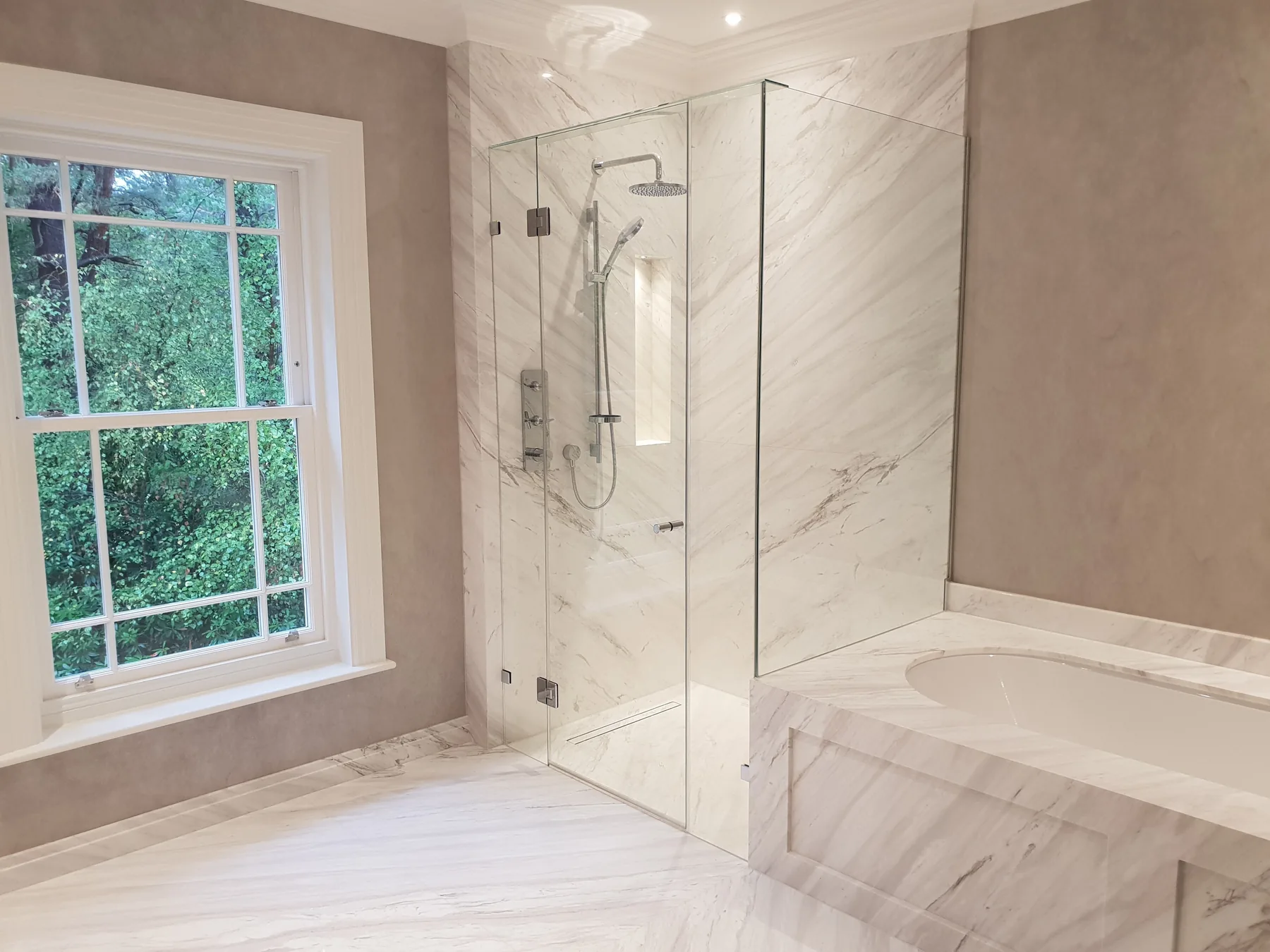 A frameless shower enclosure fitted by Fast Glass in a marble bathroom